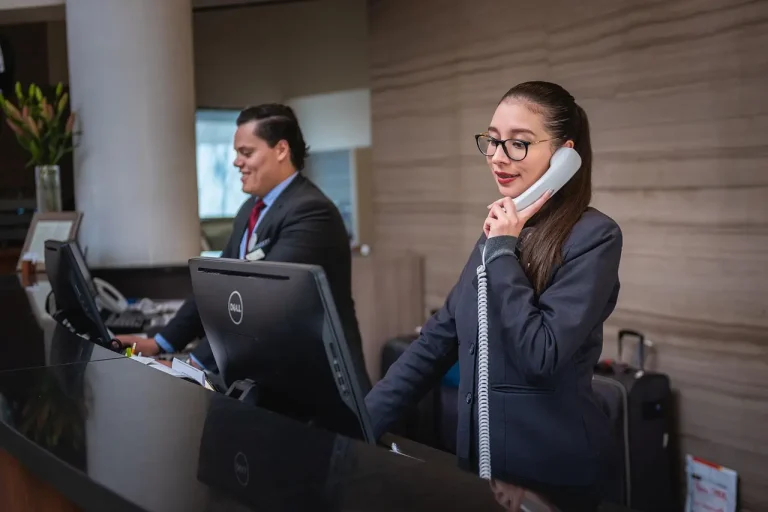 Two receptionists at the reception desk one on the phone, the other looking at the computer