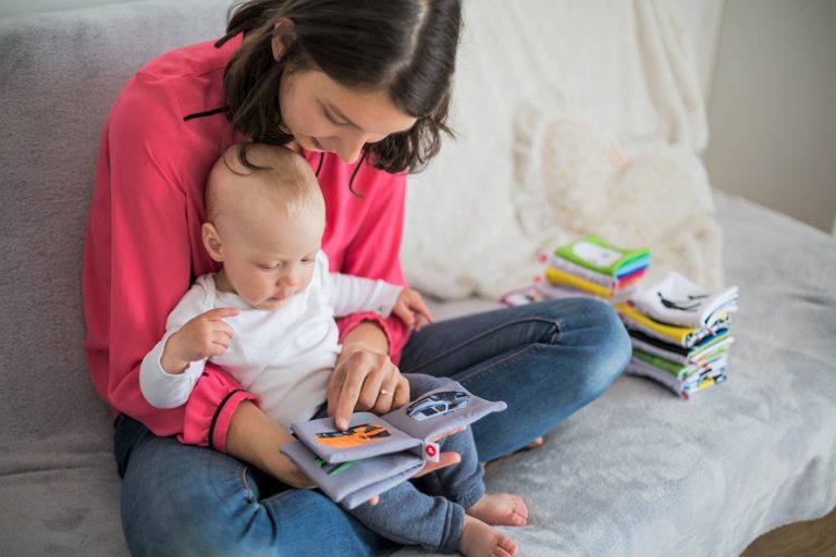 Mother sitting cross-legged on the floor reading a picture book to a child